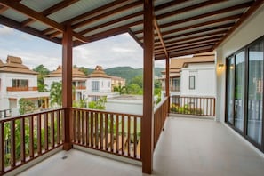 A covered balcony with a wooden railing, overlooking a residential area with houses and greenery. - Villa Palvavee (B1) (Krabi)