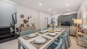 Un coin repas avec une longue table dressée pour quatre personnes, un canapé et une lampe en arrière-plan.