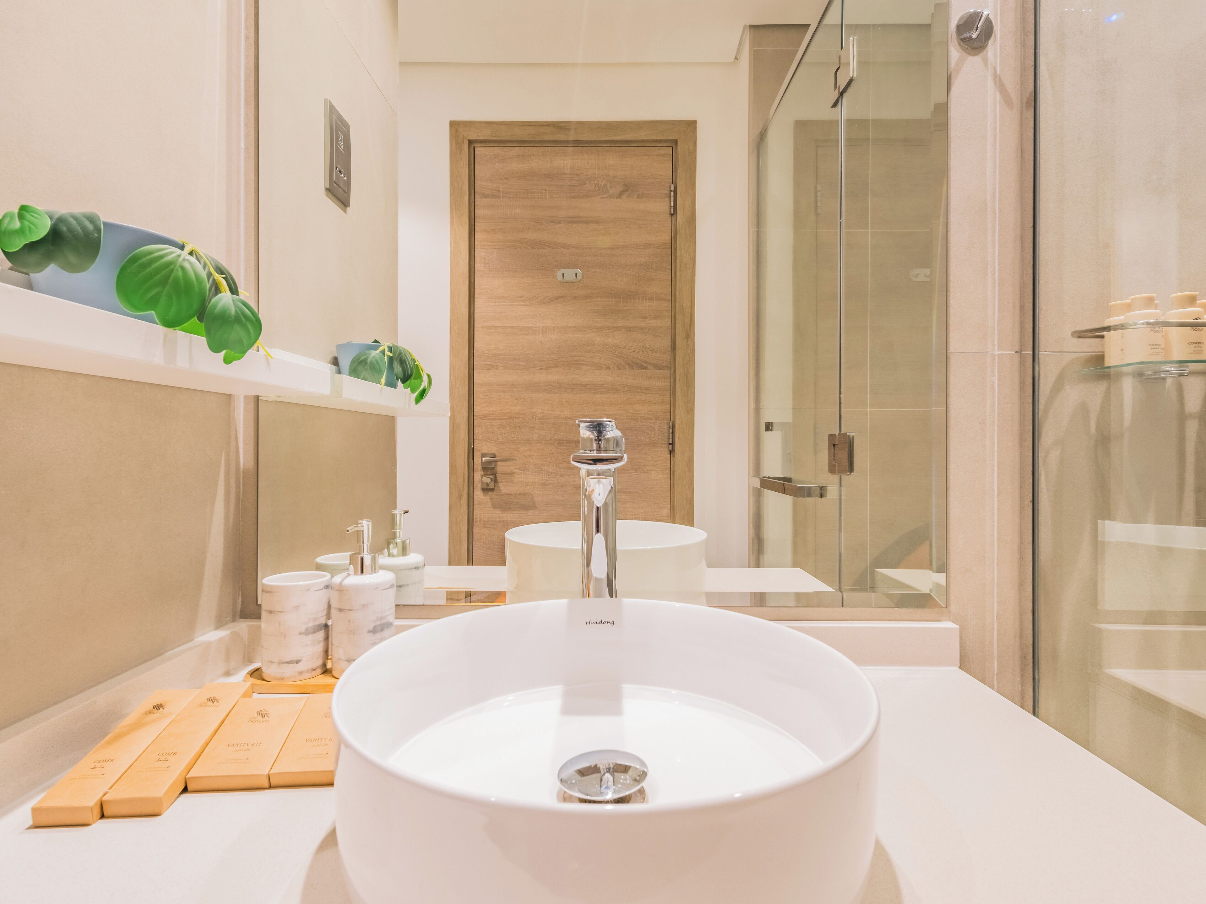 A modern bathroom with a large white sink, a wooden door, and a glass shower enclosure.