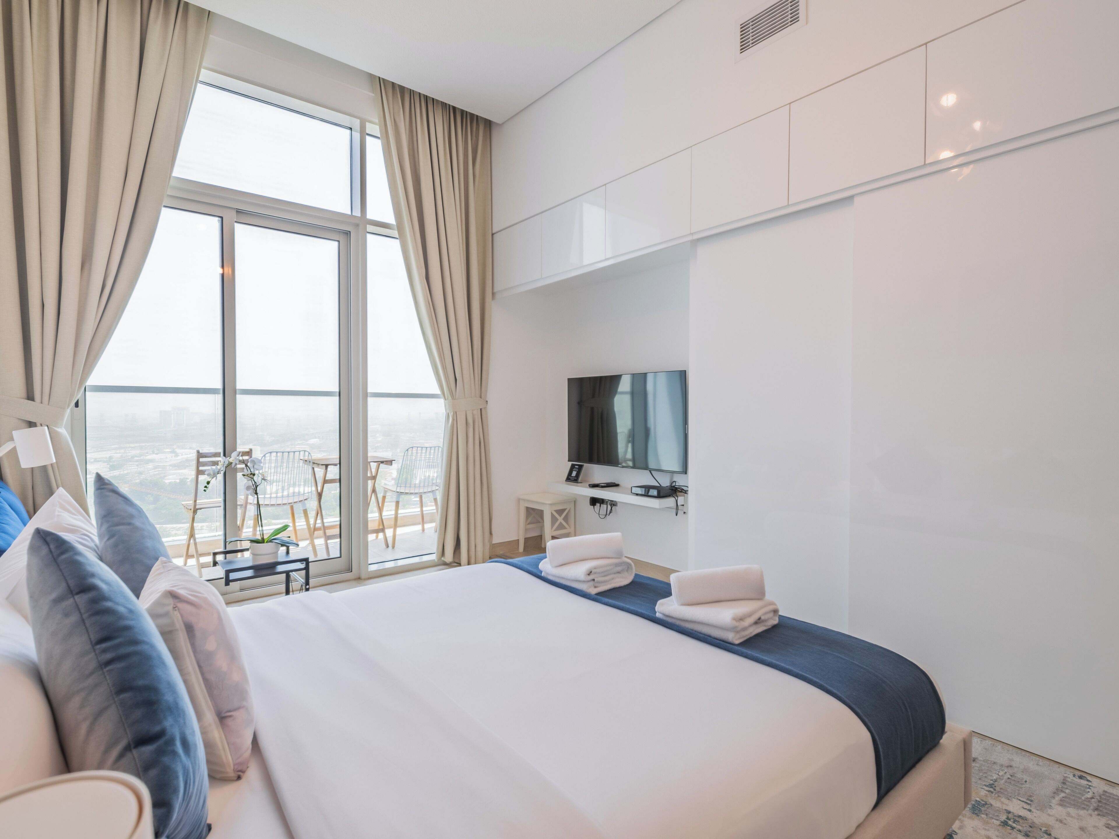 Habitación de hotel con una cama grande, un televisor montado en la pared y un balcón con vistas a la ciudad.