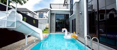 A swimming pool with a slide and inflatable swan floatation device.