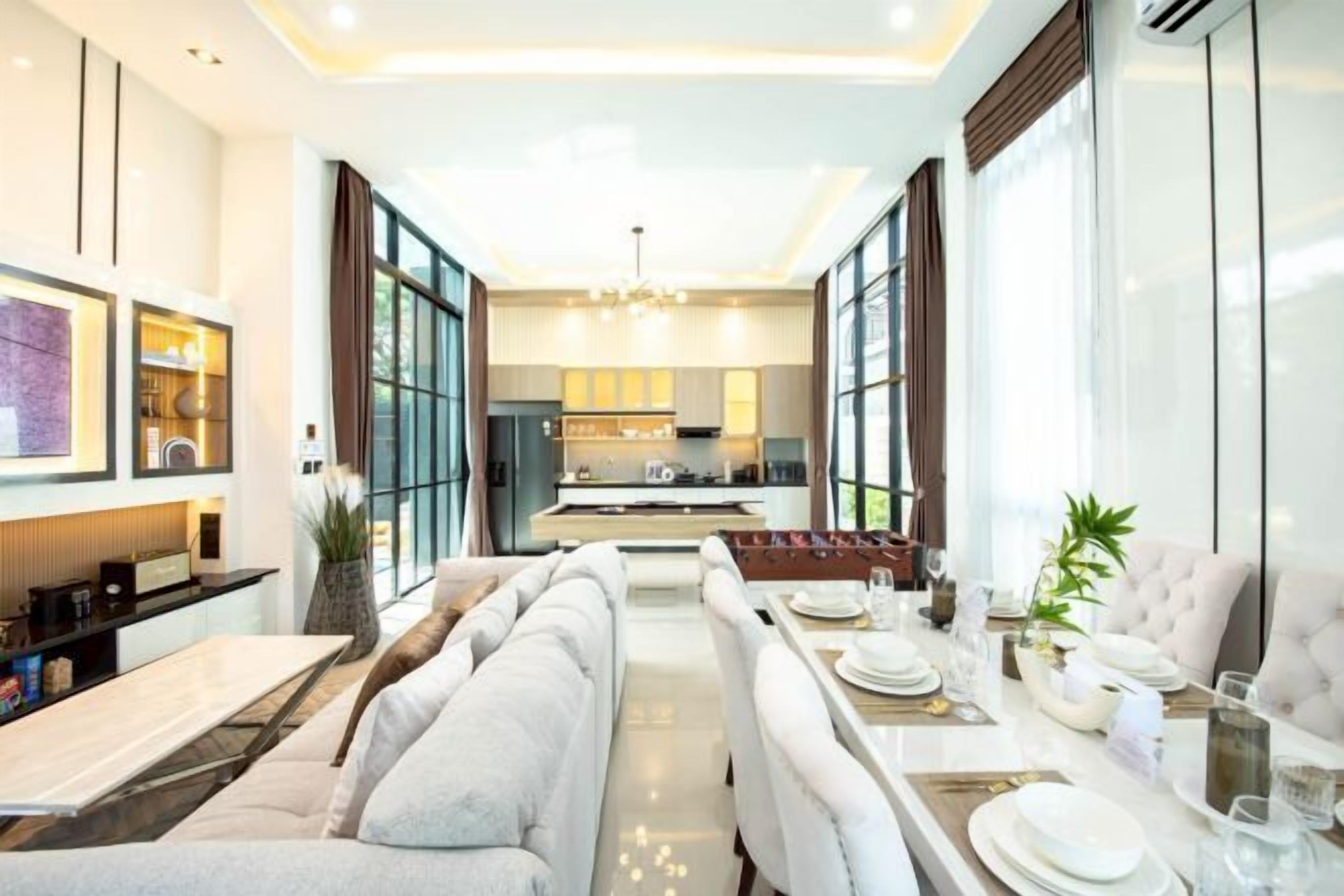 A modern hotel room with a dining area, a sofa, and a kitchen in the background.