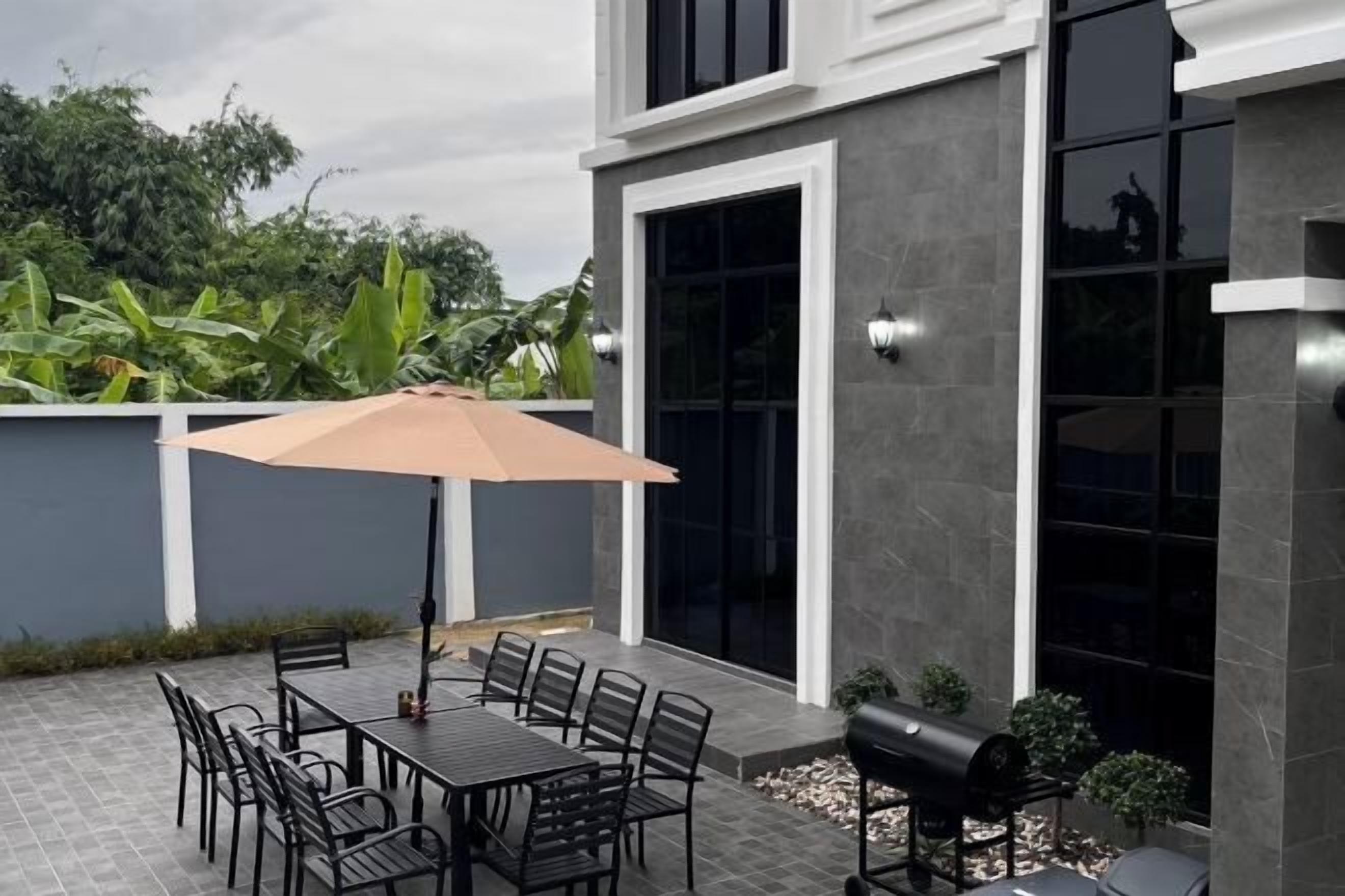An outdoor patio with a table and chairs, a barbecue grill, and a large umbrella.