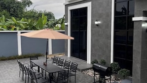 An outdoor patio with a table and chairs, a barbecue grill, and a large umbrella. - Modern 3BR British Pool Villa + 5KM Jomtien Beach (Pattaya)