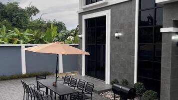An outdoor patio with a table and chairs, a barbecue grill, and a large umbrella.