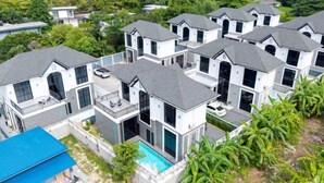 A cluster of modern houses with a swimming pool, surrounded by lush greenery. - Modern 3BR British Pool Villa + 5KM Jomtien Beach (Pattaya)