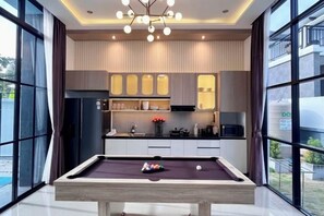 A modern kitchen with a pool table, large windows, and a view of the outside. - Modern 3BR British Pool Villa + 5KM Jomtien Beach (Pattaya)