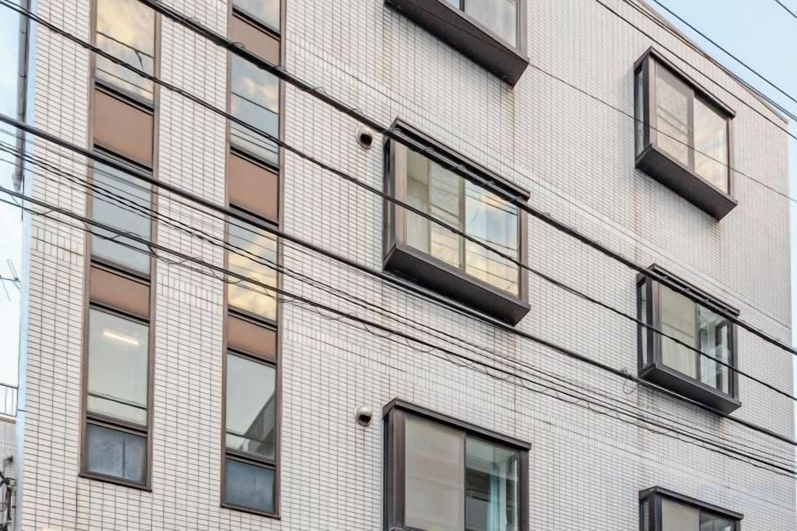A building facade with multiple windows, some with external blinds, and a tiled surface.