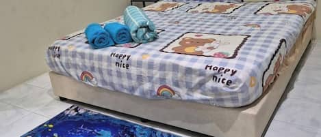 Una cama con una colcha a cuadros que presenta un personaje de dibujos animados y las palabras 'Happy Nite'. Hay toallas enrolladas sobre la cama.