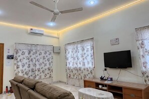 A living room with a ceiling fan, a flat-screen TV, a sofa, and curtains. - Ipoh Homestay Vacation 12 Pax 4 Bedroom for Delicious Food (Ipoh)