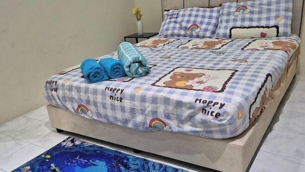 A bed with a checkered bedspread featuring 'Happy Nice' and rainbow designs, a blue towel, and a matching pillow. - Ipoh Homestay Vacation 12 Pax 4 Bedroom for Delicious Food (Ipoh)