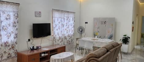 Una sala de estar con sofá, televisor, mesa de comedor y cortinas.