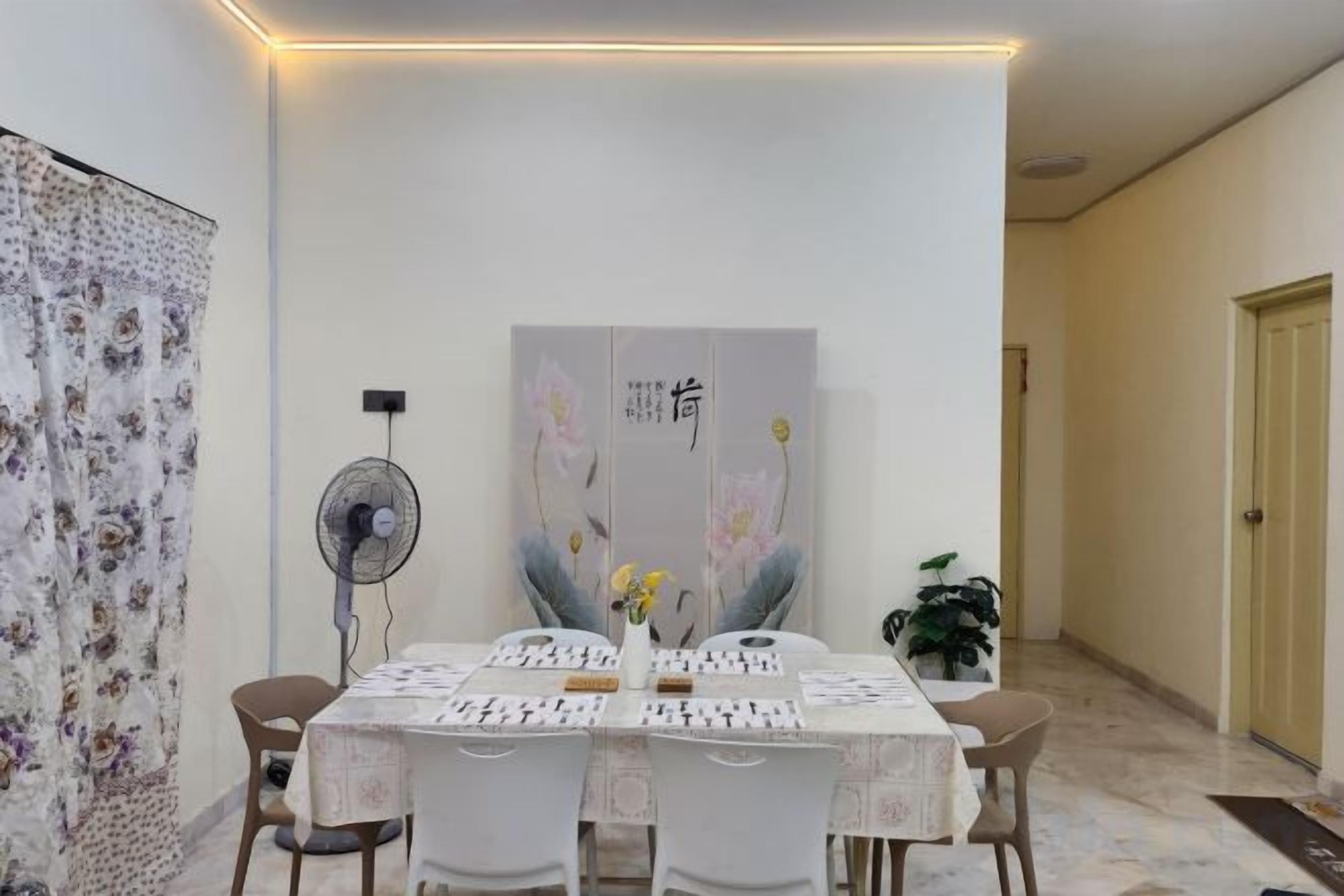 A dining area with a table set for four, a fan, and a large decorative painting on the wall.
