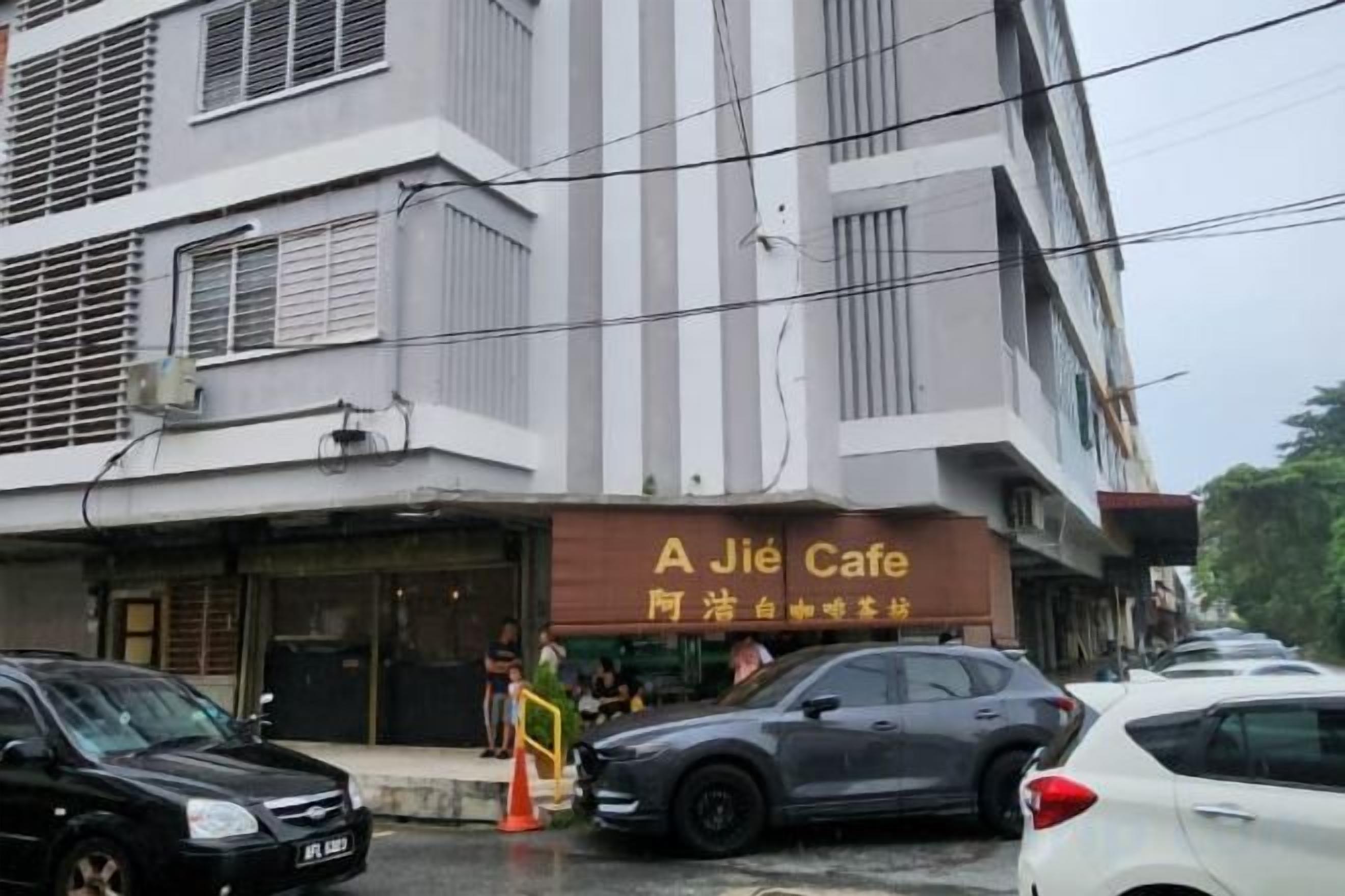 Um edifício com um café chamado 'A Jié Cafe' no andar térreo. Há carros estacionados na frente e uma pessoa visível perto da entrada.
