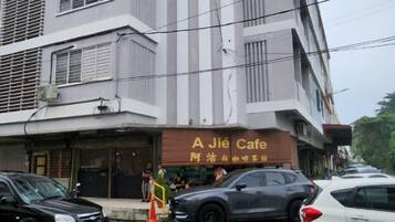 Um edifício com um café chamado 'A Jié Cafe' no andar térreo. Há carros estacionados na frente e uma pessoa visível perto da entrada.