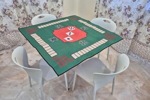 Mesa com toalha verde e padrões vermelhos e brancos, rodeada por cadeiras brancas.