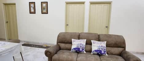 A room with a brown sofa, two pillows, a white table, and two doors.
