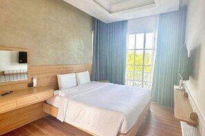 A hotel room with a large bed, a wooden bedside table, a built-in TV, and a window with curtains. - Novaworld Phan Thiet - QT Villa (Phan Thiet)
