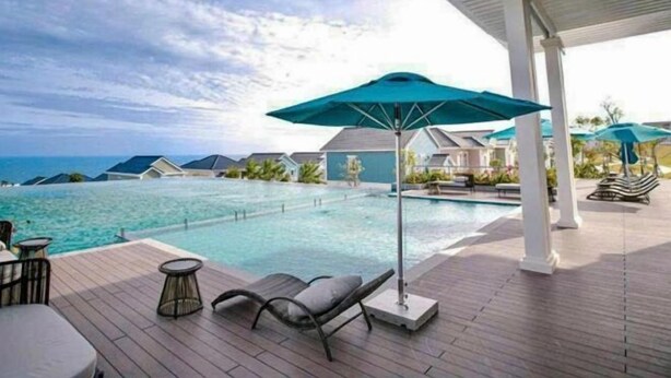 A poolside area with lounge chairs, umbrellas, and a view of the ocean.