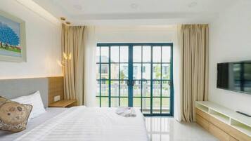 A hotel room with a bed, a TV, a window with curtains, and a painting on the wall.