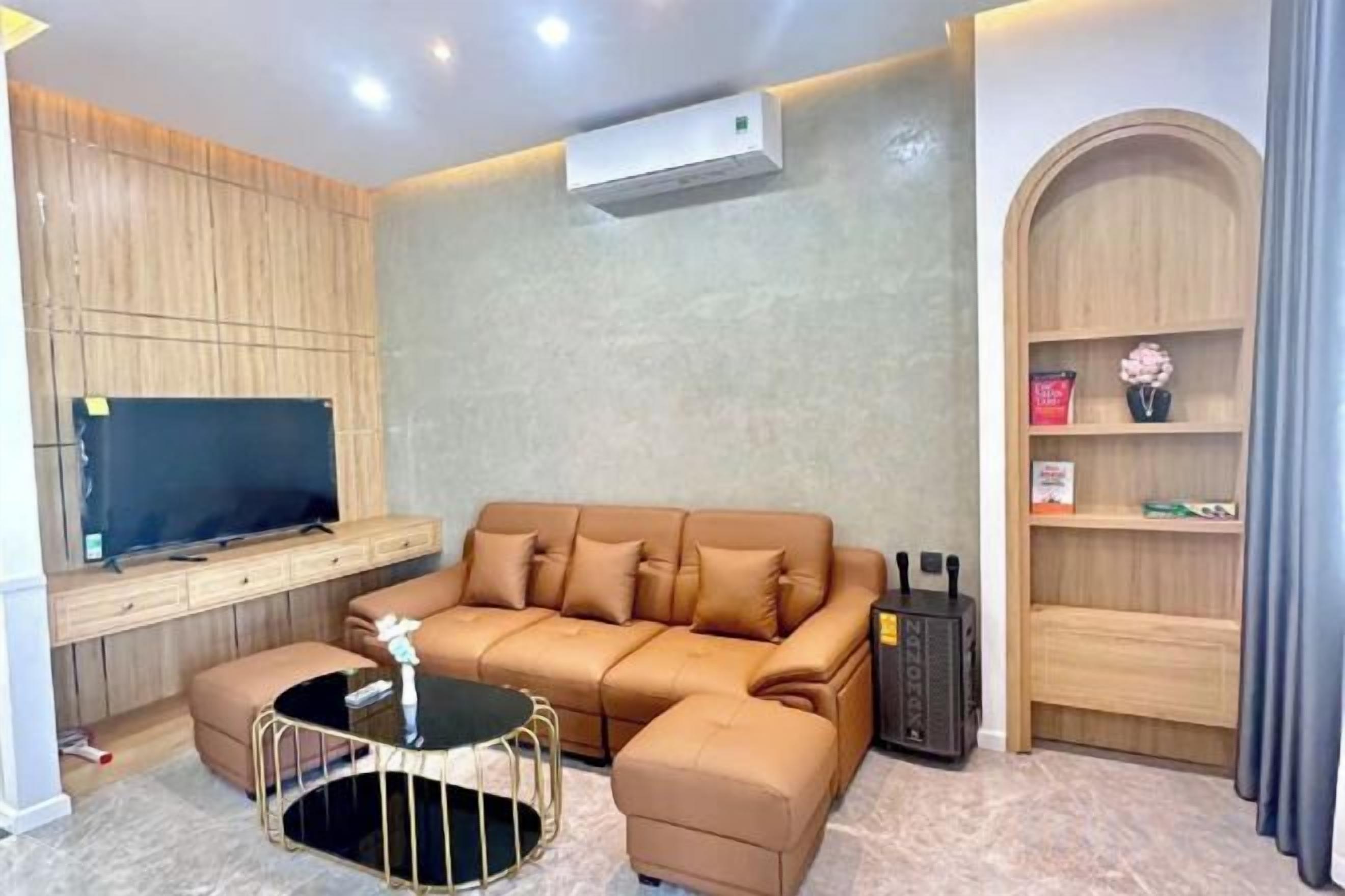 Een moderne woonkamer met een hoekbank, een salontafel, een flatscreen televisie en een inbouwkast met decoratieve objecten.