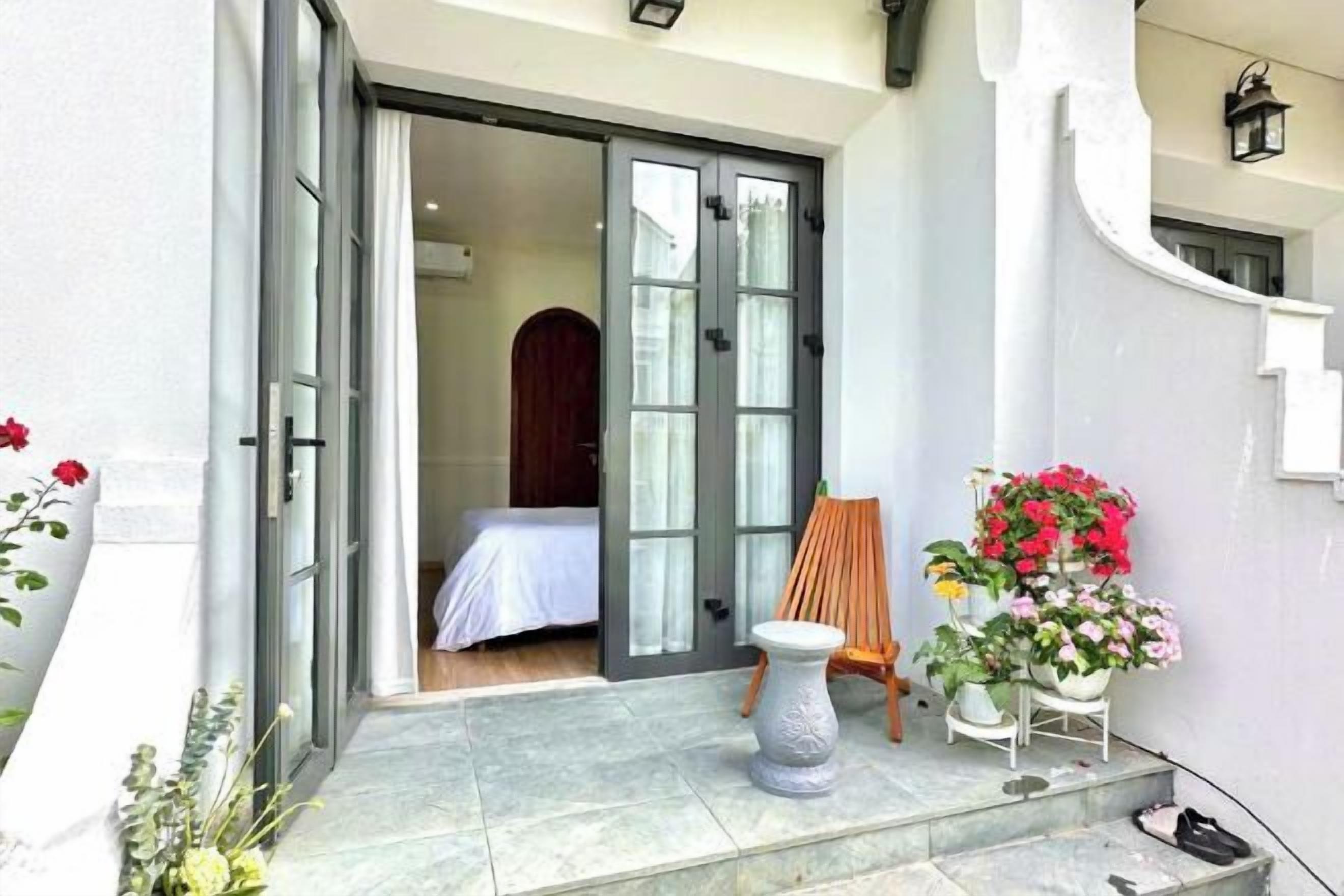 A hotel entrance with a sliding glass door, a small seating area with a chair and a table, and potted plants.