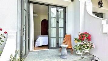 A hotel entrance with a sliding glass door, a small seating area with a chair and a table, and potted plants.