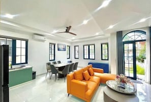 A modern living room with a sofa, dining table, chairs, and a kitchen area.