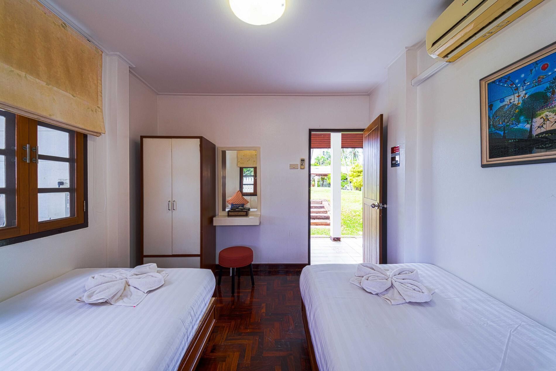 A hotel room with two beds, a wardrobe, a desk with a chair, and a painting on the wall.