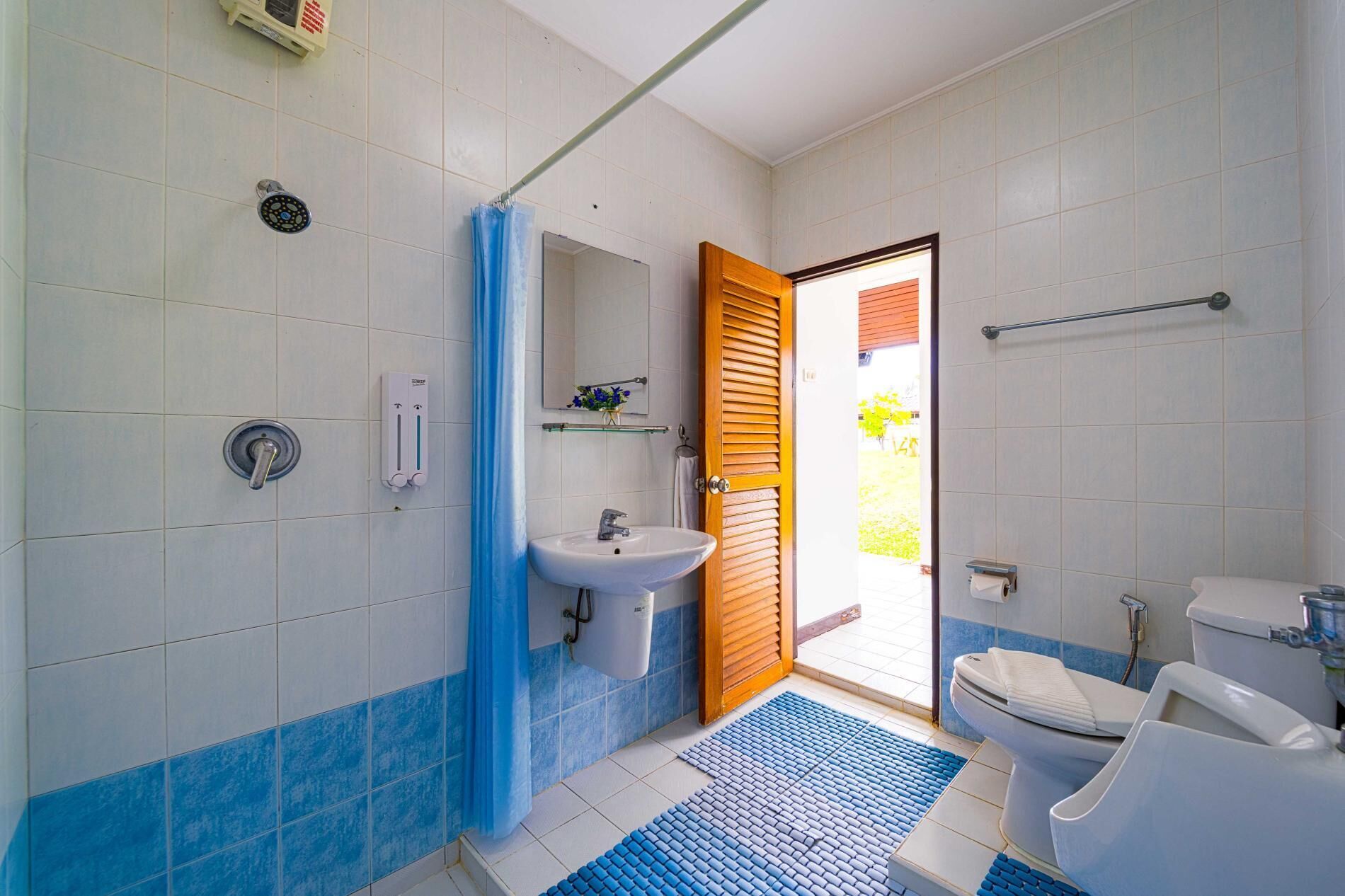 Et badeværelse med bruser, vask, toilet og en trædør, der fører ud til en balkon.