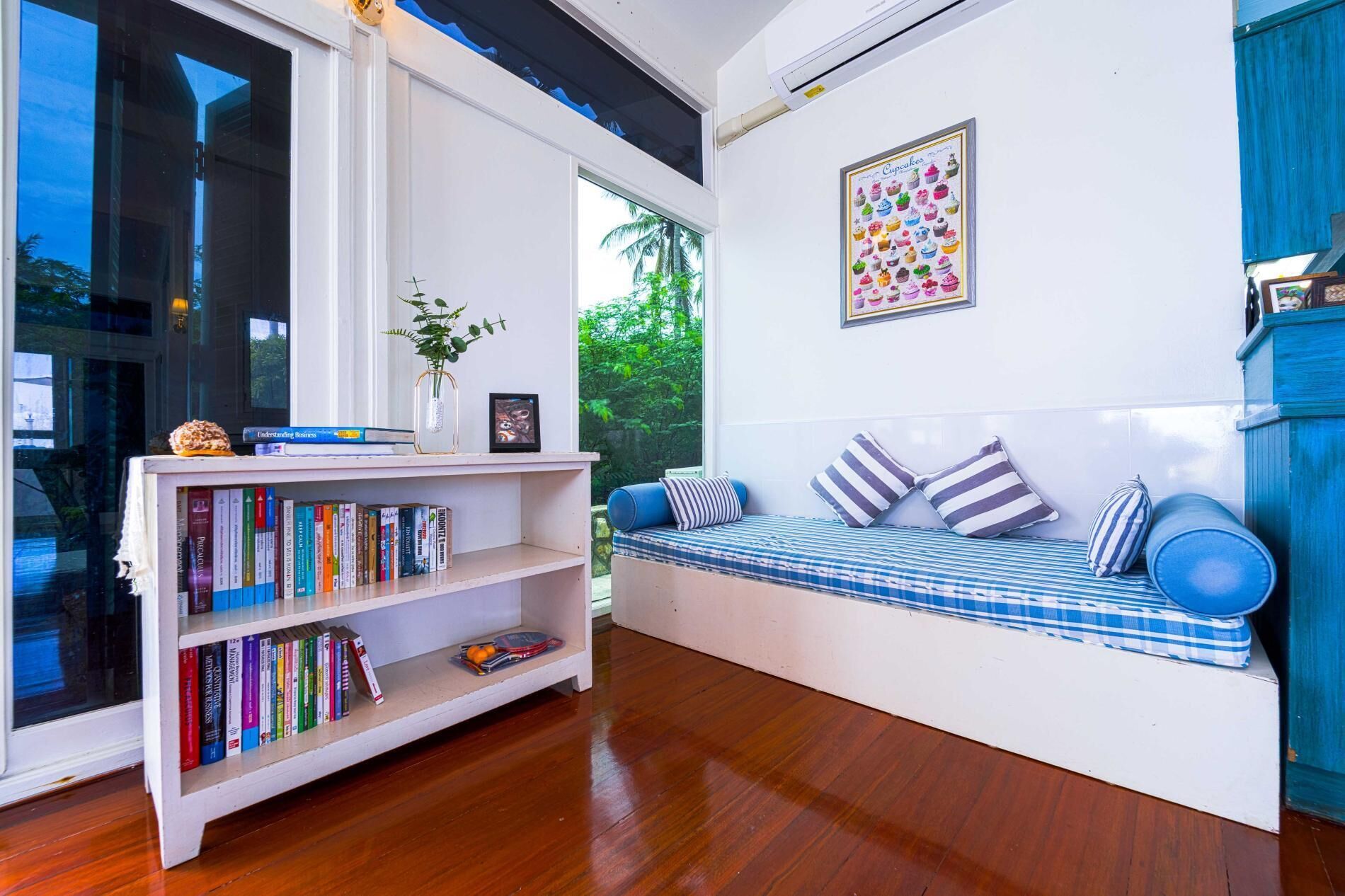 A modern living room with a white bookshelf, a blue sofa with striped cushions, and a framed picture of cupcakes on the wall.