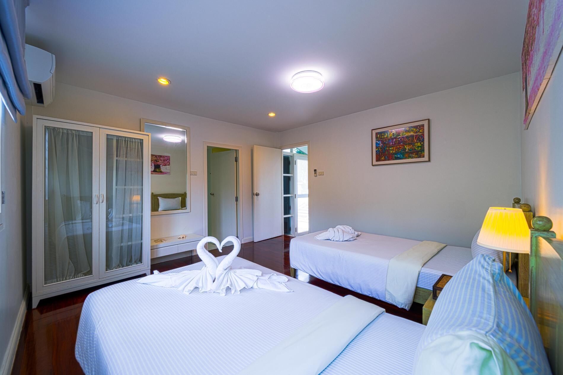 Una habitación de hotel con dos camas, un armario, un espejo, un cuadro y una lámpara.