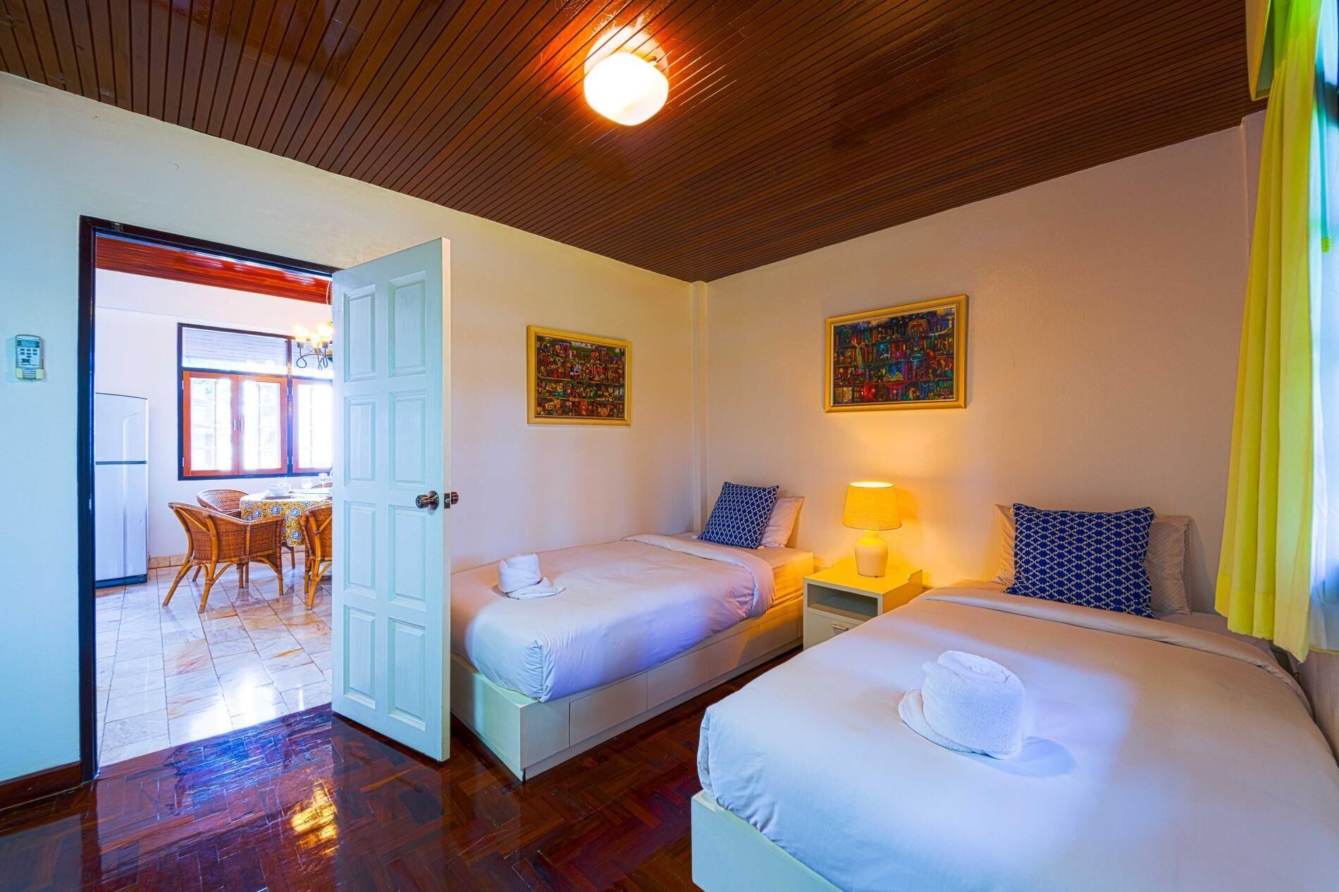 A hotel room with two beds, a dining area, and a kitchen visible through an open door.