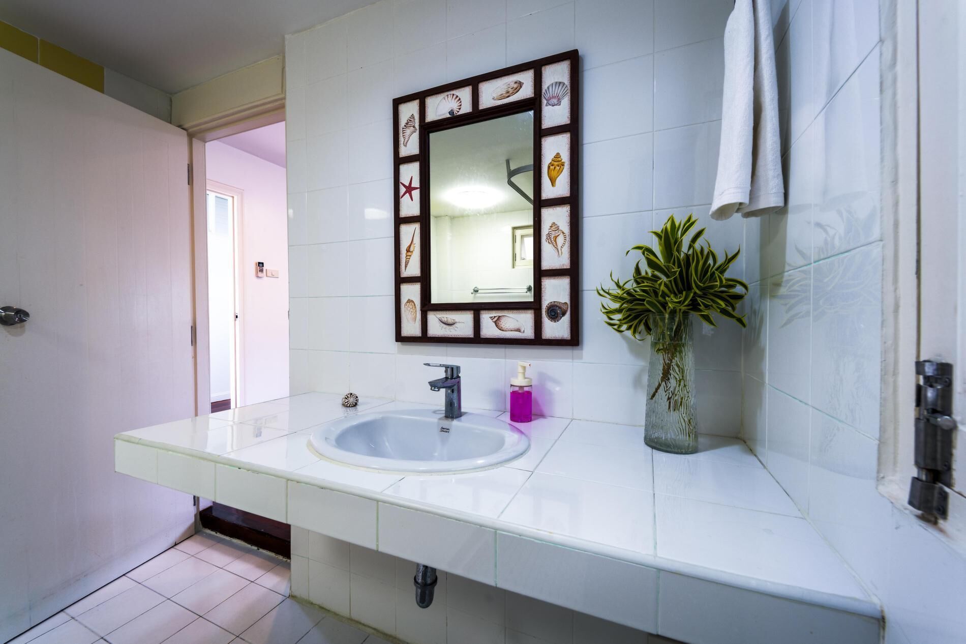 A bathroom with a white sink, a mirror with a decorative frame, a plant, and a towel hanging on the wall.