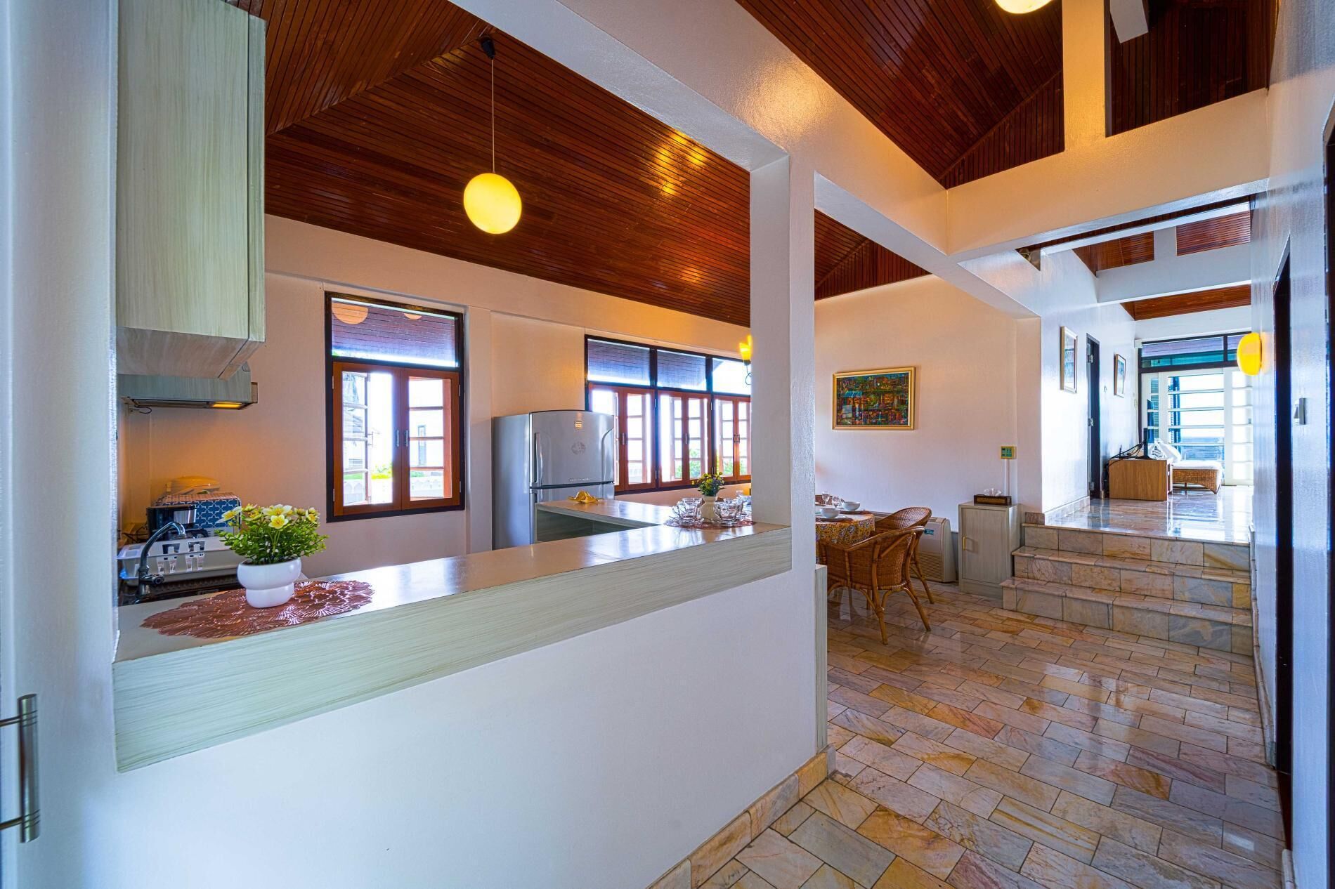 A modern kitchen with a central island, wooden ceiling, and large windows.