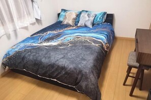 Un lit recouvert d’une couvre-lit à motifs bleus et noirs, une chaise en bois et un rideau blanc.