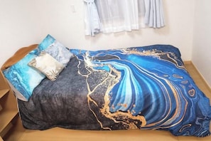 A bed with a blue and black patterned bedspread, a wooden headboard, and a white pillow.