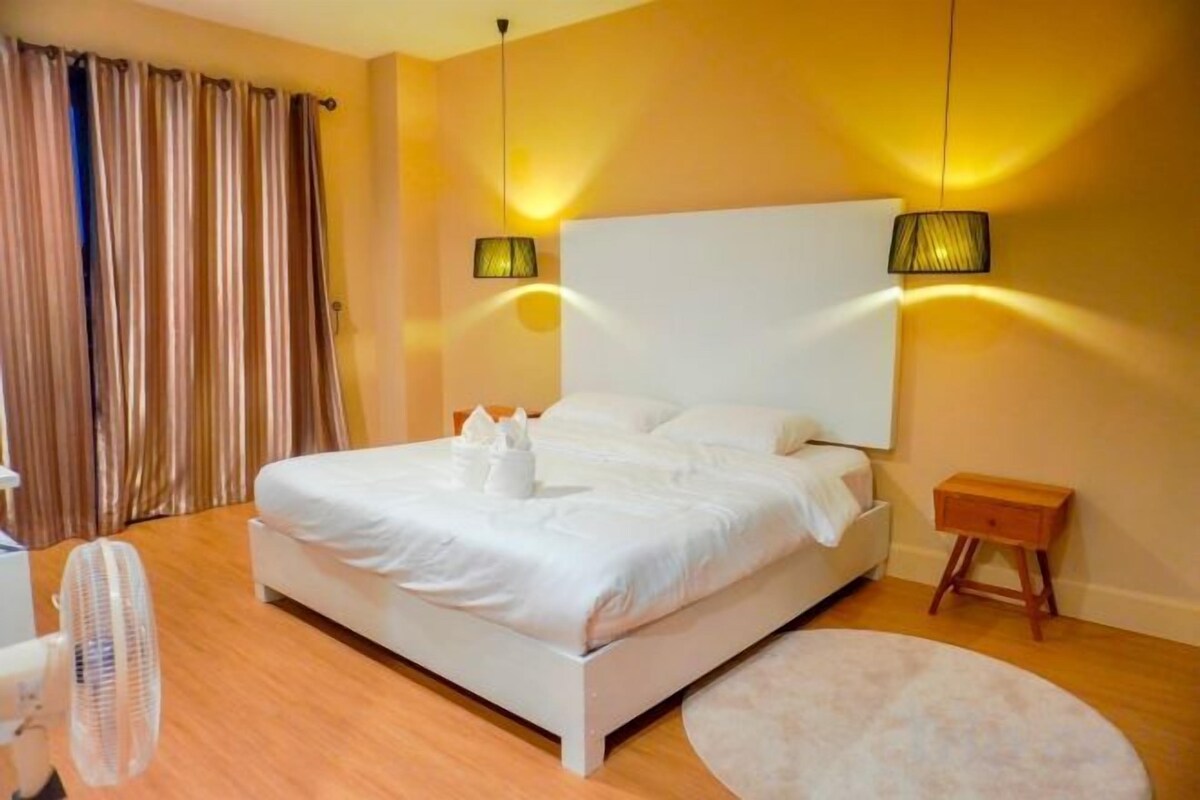 A hotel room with a large bed, bedside lamps, a small wooden nightstand, and a round rug.