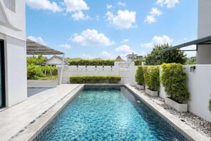 Une piscine rectangulaire à l’eau d’un bleu limpide, entourée d’une terrasse carrelée de couleur blanche et de petites haies.