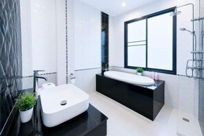 Een moderne badkamer met een grote witte wastafel, een zwart aanrecht en een inloopdouche.
