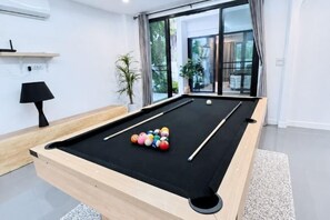 Une table de billard dans une pièce moderne, avec une grande fenêtre, une lampe et une plante.