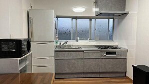 Une cuisine compacte équipée d’une cuisinière intégrée, d’un four à micro-ondes et d’un réfrigérateur. Une fenêtre se trouve au-dessus de l’évier, et les murs de la pièce sont peints en blanc, tandis que le sol est recouvert de parquet.