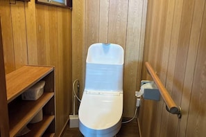 Ein kleines Badezimmer mit Holzwandverkleidung, einer weißen Toilette, einem Holzbodenregal und einer Handstange.