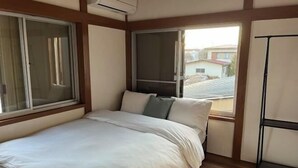 Une chambre à coucher avec un lit, deux fenêtres et une vue sur un quartier résidentiel.