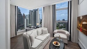A modern hotel room with a large window offering a city view, a sofa, a chair, and a small table with a fruit bowl. - La Clef Bangkok by The Crest Collection (Bangkok)