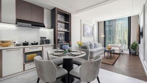 A modern kitchen with white cabinets, a dining area with a round table, and a living room with a sofa and a coffee table. - La Clef Bangkok by The Crest Collection (Bangkok)