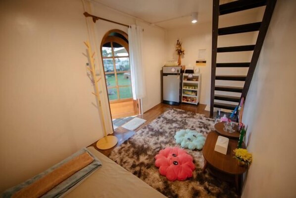 A cozy room with a wooden floor, a small table with a vase, and a staircase. - With You Camp (Sirindhorn)