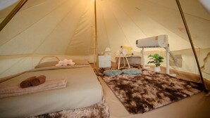 A tent with a bed, a small table, a lamp, and a heater. - With You Camp (Sirindhorn)