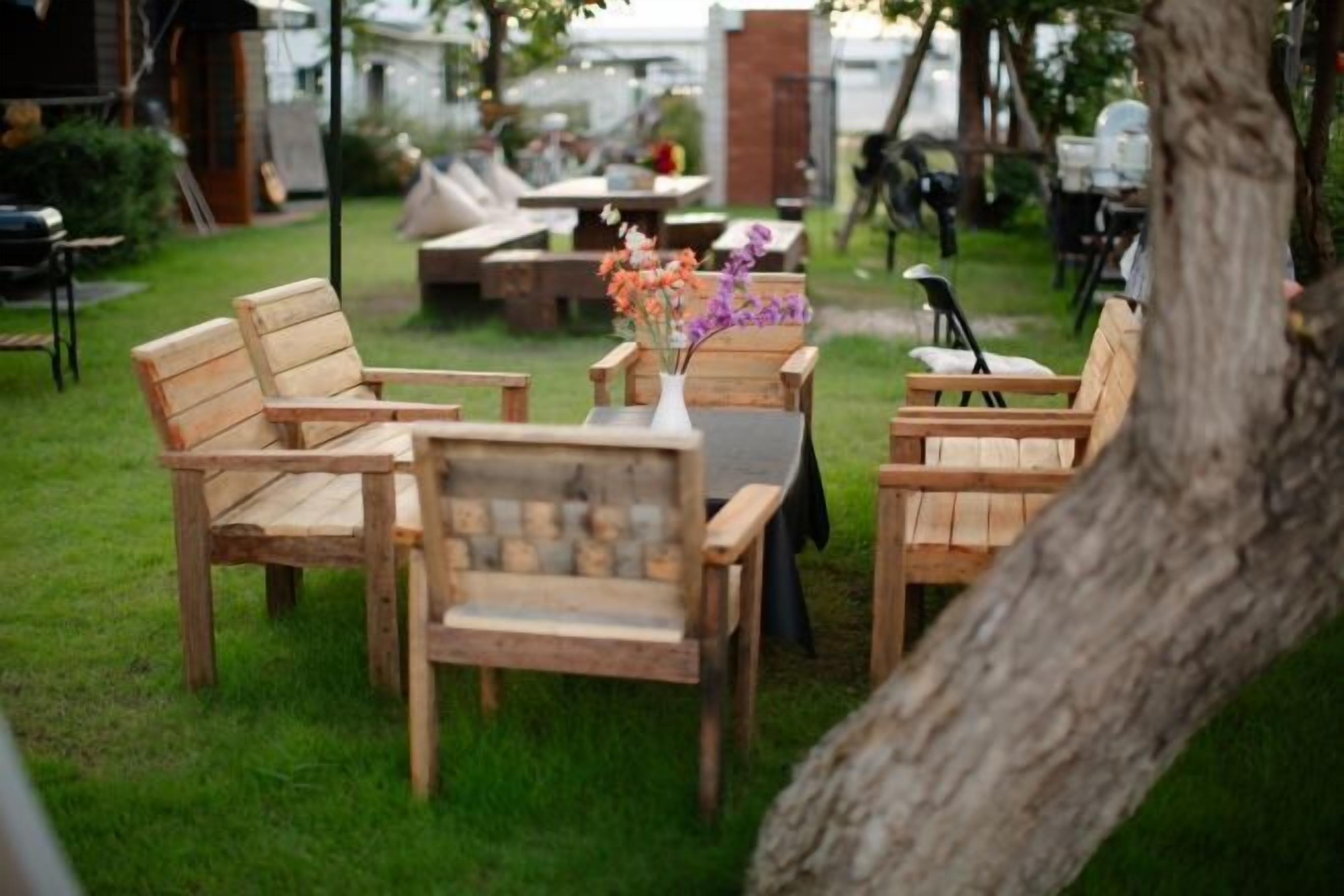 A wooden outdoor seating area with a table and chairs, surrounded by greenery.