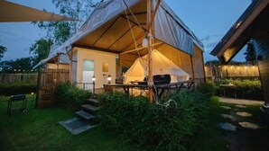 A tented accommodation with a patio area, steps leading to the entrance, and a small table with chairs. - With You Camp (Sirindhorn)